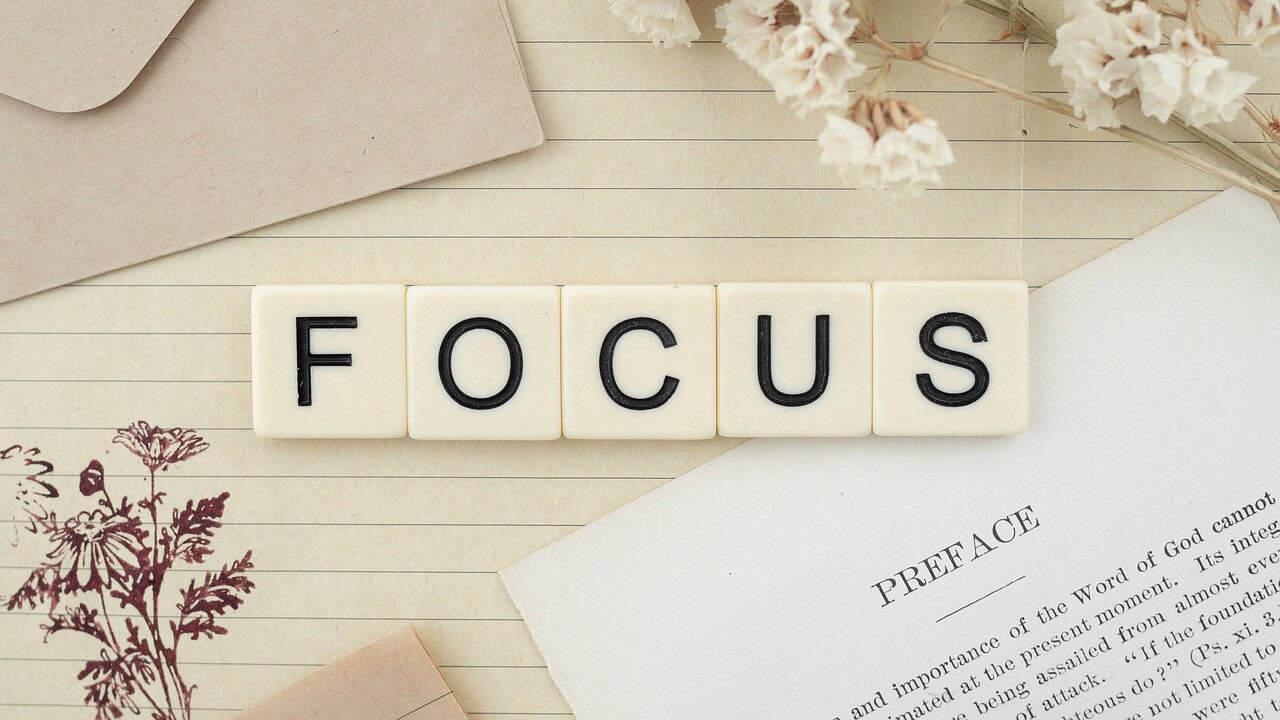 Visualising the focus required for professional writing: Scrabble tiles spelling 'FOCUS' over a printed book preface, representing the habit of reading well-written material to improve memory and credibility.