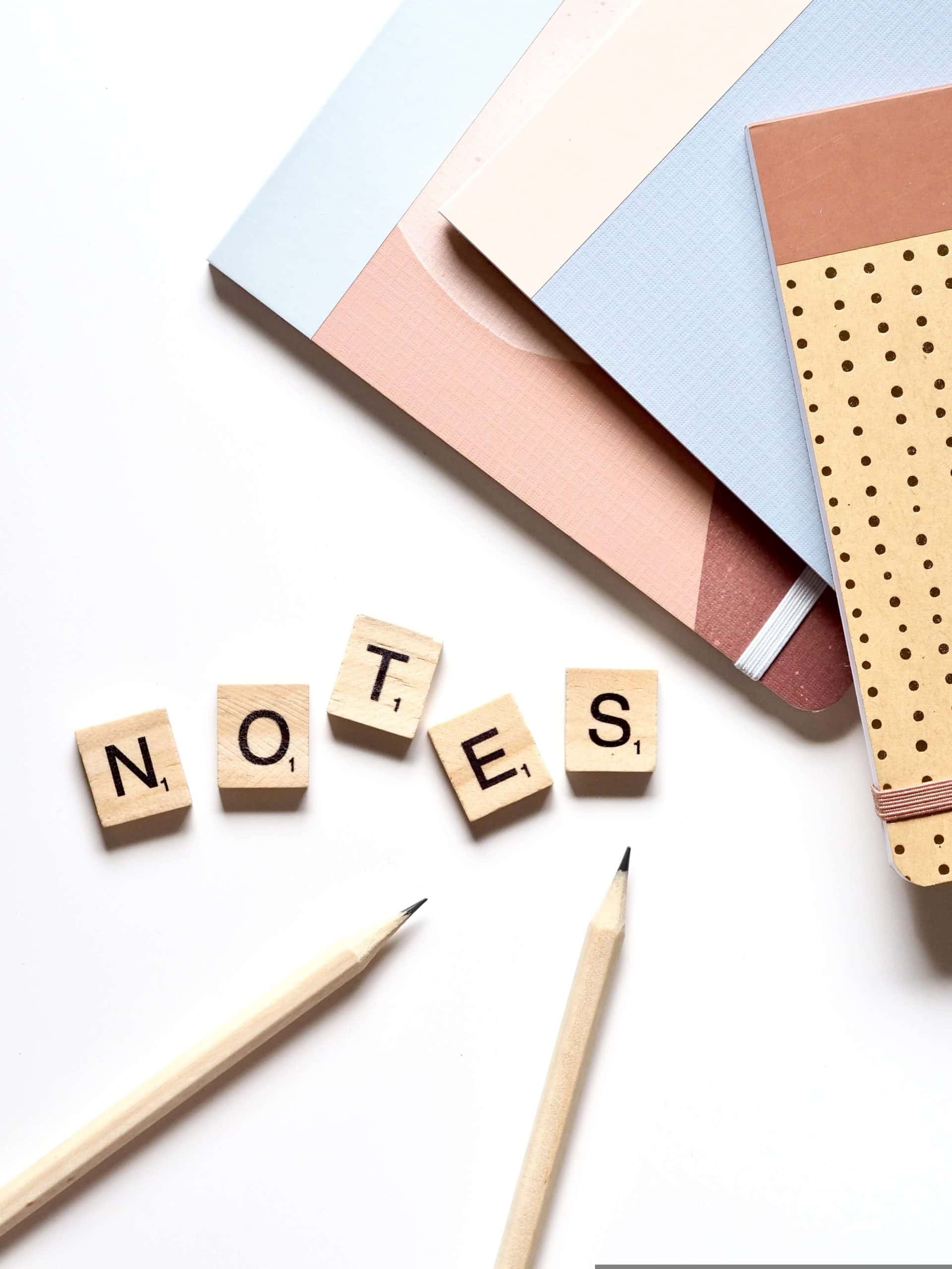 Notebooks, pencils, and wooden letter tiles spelling 'NOTES', representing the planning and organisation needed for effective business writing.